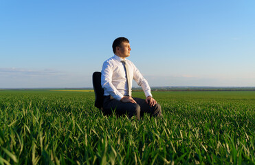 Naklejka na ściany i meble businessman sits in an office chair in a field and rests, freelance and business concept, green grass and blue sky as background