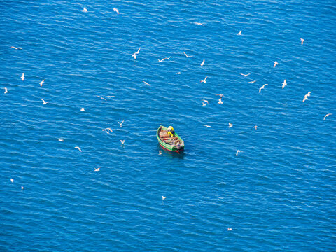 A Lone Boat With Industrial Fishermen In The Open Sea With A Rod And Nets. The Concept Of Poaching And Illegal Fishing.