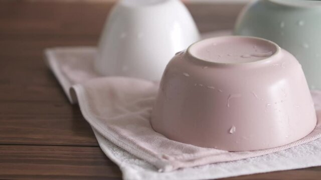 Clean damp dishes on a tea towel. Crockery in pastel pink and green. Ceramic tableware in pastel colors. Three different empty smoothie bowls. Eco and minimalist home still life. Woman hands puts rins