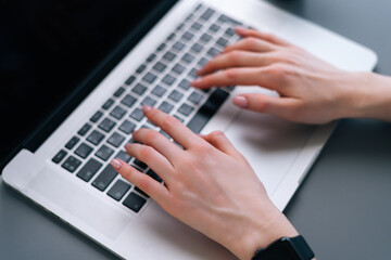 Close-up hands of unrecognizable business woman working typing on laptop notebook keyboard sitting at desk on background of window in dark office room, selective focus.
