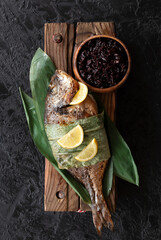 grilled dorada fish in bamboo leaves and black rice. Top view