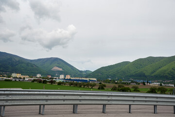 Fototapeta premium Highway fence in the mountain landscape. Village with houses and buildings