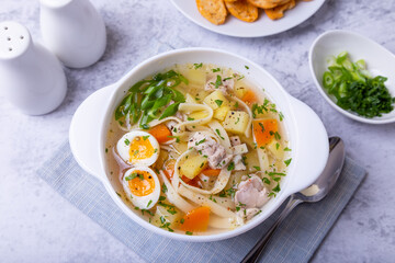 Soup with chicken, noodles, potatoes, quail eggs and carrots. Seasoned with onions and parsley. Close-up.