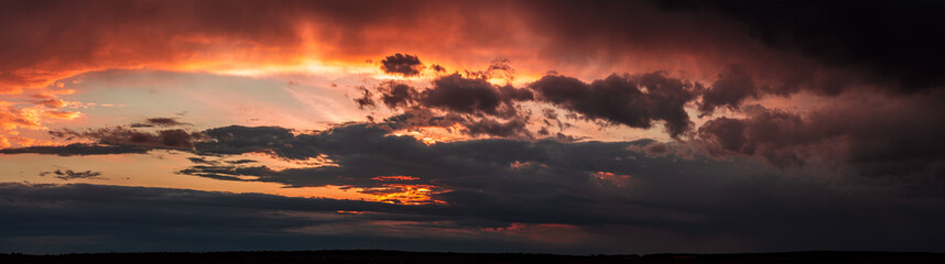 Dramatic dark sunset. Panorama of dark rain clouds in the evening. A rich red sky before a night thunderstorm