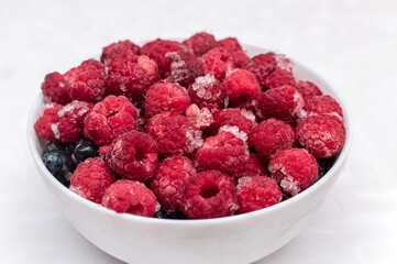 Frozen Summer Berries in a Bowl - Tasty Raspberries and blueberries. Bowl with frozen ripe berries on a white table