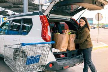 woman put bags with products in car trunk after grocery store