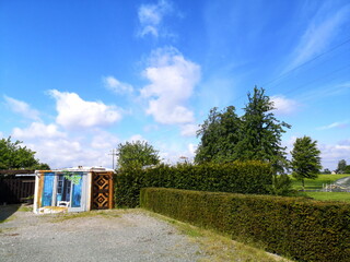 Schotterparkplatz mit bemaltem Garagentor und grünen Hecken im Sommer bei Sonnenschein in der...