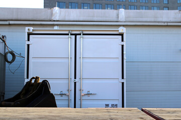 Narrow white cargo container, a loading area in the foreground, a workshop hall in the background.