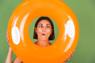 Summer fit sporty woman in pink bikini and bright orange inflatable ring round on green background, happy playful with funny grimaces