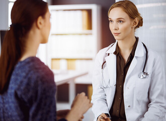 Cheerful smiling female doctor and patient woman discussing current health examination while...