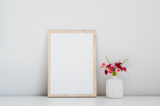 Wooden photo frame poster and vase with fresh flowers on white table