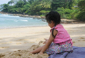 side view of a little cute girl dress casually sitting on the beach playing sand. Holiday, family, healthy child concept