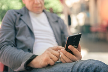 Middle aged man in jacket and white t-shirt using smartphone while sitting in cafe