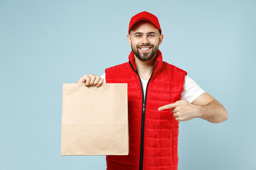 Delivery guy employee man in red cap white T-shirt vest uniform work as dealer courier service hold brown clear blank craft paper takeaway bag mock up isolated on pastel blue color background studio.