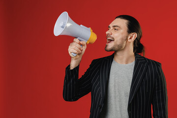 Young happy expressive fun successful businessman latin man 20s wearing black striped jacket grey shirt scream in megaphone announces discounts sale hurry up isolated on red color background studio
