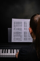 Rear view of young girl practicing the piano in solemn dark atmosphere having the left hand on the...
