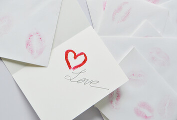 Love card with a red heart shape drew by lipstick and handwritten word Love in the back ground of white envelopes with kisses lipstick marks.