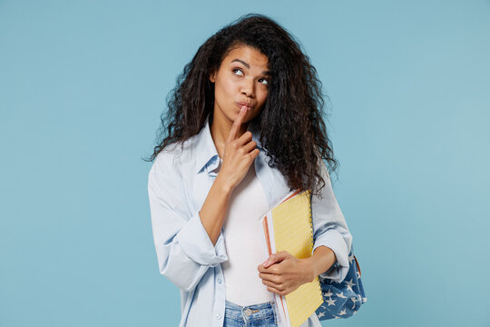Young thoughtful pensive african american girl teen student in denim clothes backpack hold book prop up chin look aside isolated on blue background Education in high school university college concept