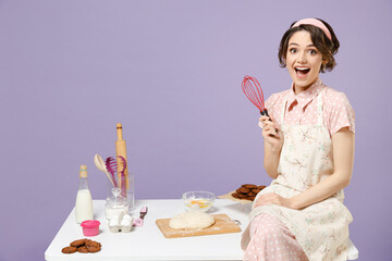 Young amazed excited happy housewife housekeeper cook chef baker woman in apron work sit on table...
