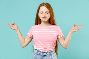 Little redhead spiritual kid girl 12-13 years old wearing pink striped t-shirt spread hands in yoga...