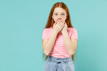 Little shocked surprised redhead kid girl 12-13 years old wear pink striped t-shirt cover mouth with hands arms isolated on pastel blue background studio portrait Children lifestyle childhood concept