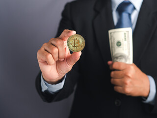 Hand of a businessman showing a bitcoin golden coin and holding US dollars banknotes while standing with a gray background. Close-up photo. Virtual cryptocurrency and future money concept
