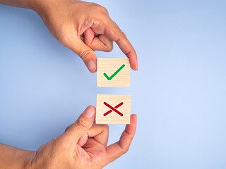 Hand of holding green checkmark and red cross symbol on wooden blocks on light blue background. Top...