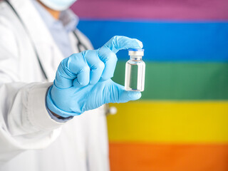 Hand of a doctor holding a vaccine bottle against the background of the rainbow flag (LGBT). Vaccine for immunization and treatment from virus infection. Space for text