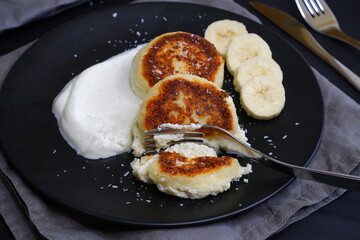Curd pancakes in a black plate and on a black background.