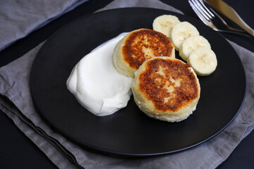 Curd pancakes in a black plate and on a black background.