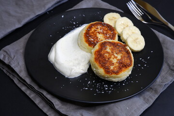 Curd pancakes in a black plate and on a black background.