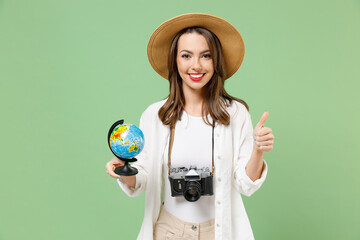 Traveler fun tourist woman in casual clothes hat camera spin touch Earth world globe show thumb up isolated on green background Passenger travel abroad on weekends getaway. Air flight journey concept.
