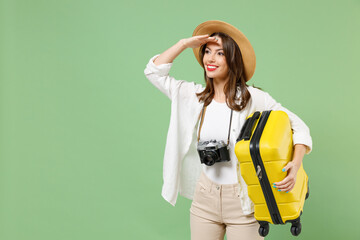 Traveler waiting tourist woman in casual clothes hat hold yellow suitcase valise look far away distance isolated on green background Passenger travel abroad weekend getaway Air flight journey concept - obrazy, fototapety, plakaty