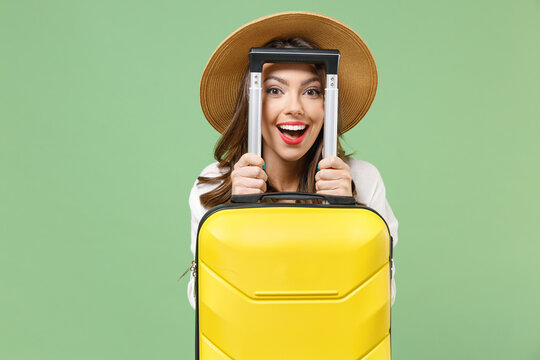 Close up satisfied fun traveler tourist woman in casual clothes hat hiding with yellow suitcase valise isolated on green background Passenger travel abroad weekend getaway Air flight journey concept