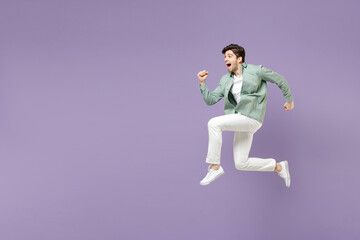 Fototapeta na wymiar Full length side view excited amazed fun young man in casual mint shirt white t-shirt jump high running fast hurrying up look camera isolated on purple violet background. People lifestyle concept