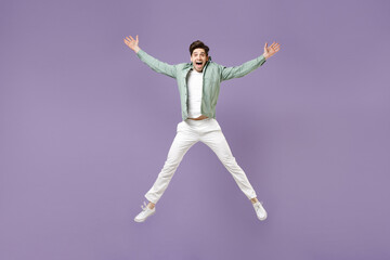 Fototapeta na wymiar Full length fun excited overjoyed amazed cool young man in casual mint shirt white t-shirt jump high with outstretched hands look camera isolated on purple violet background. People lifestyle concept
