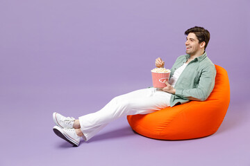 Full length fun happy man 20s in casual mint shirt white t-shirt sitting in orange bean bag chair...