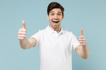 Young fun happy smiling unshaven cheerful caucasian man 20s wear white casual basic t-shirt show thumbs up gesture isolated on pastel blue color background studio portrait. People lifestyle concept.