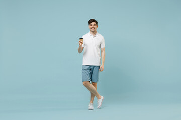 Fototapeta na wymiar Full size young happy fun man 20s in white casual basic t-shirt hold takeaway delivery craft paper brown cup coffee to go isolated on pastel blue background studio portrait People lifestyle concept
