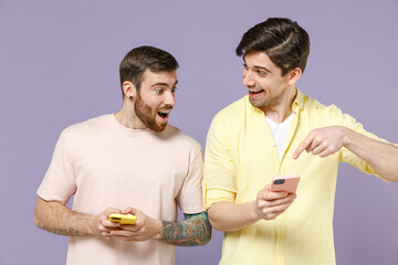 Young smiling cool happy men friends together in casual t-shirt tattoo translate fun hold mobile cell phone chat online point index finger show isolated on purple background People lifestyle concept
