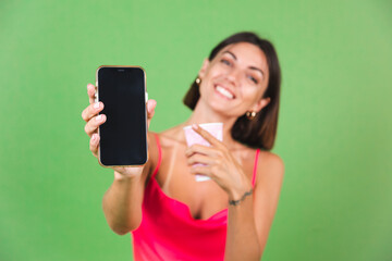Stylish woman in pink silk dress isolated on green background happy excited point on black empty mobile phone screen