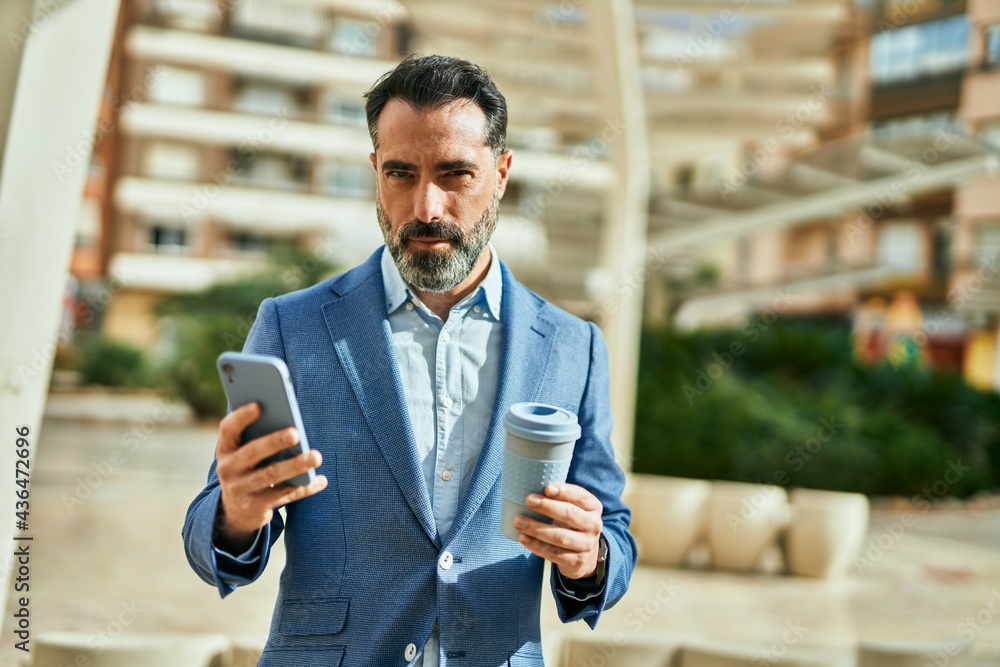 Wall mural Middle age businessman using smartphone and drinking coffee at the city.