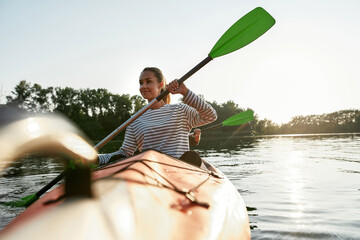 Cheerful young woman enjoying kayaking with her friend in a lake on a summer day