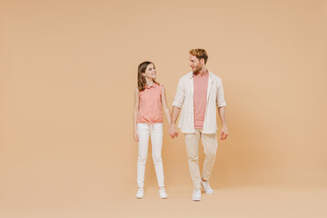 Full length cool young parent man have fun with cute child teen girl in casual pastel clothes. Daddy little kid daughter walk hold hands isolated on beige background. Father's Day Love family concept.