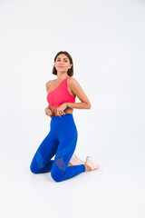 Fit tanned sporty woman with abs, fitness curves, wearing top and blue leggings on white background