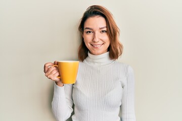 Young caucasian woman holding coffee looking positive and happy standing and smiling with a confident smile showing teeth