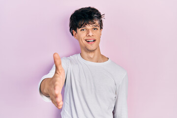 Handsome hipster young man wearing casual white shirt smiling friendly offering handshake as greeting and welcoming. successful business.