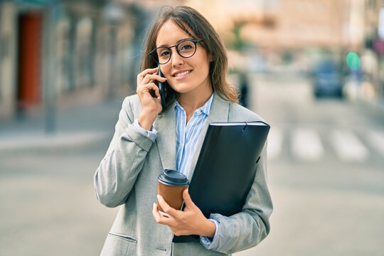 Young hispanic businesswoman talking on the smartphone and drinking take away coffee at the city.