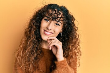 Young hispanic girl wearing casual clothes smiling looking confident at the camera with crossed arms and hand on chin. thinking positive.