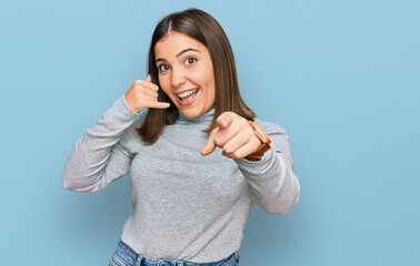 Young beautiful woman wearing casual turtleneck sweater smiling doing talking on the telephone gesture and pointing to you. call me.